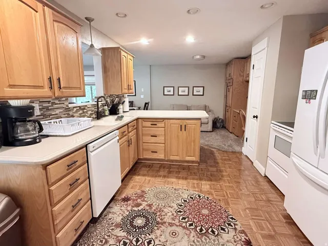 Kitchen featuring wood-finish flooring, wood cabinetry with dark hardware, a peninsula with counter seating, a tile backsplash, and a white dishwasher