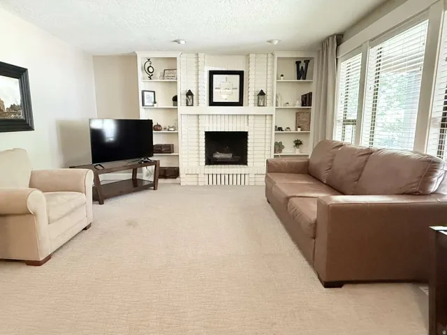 White brick fireplace with built-in shelving, large windows with blinds, and recessed lighting
