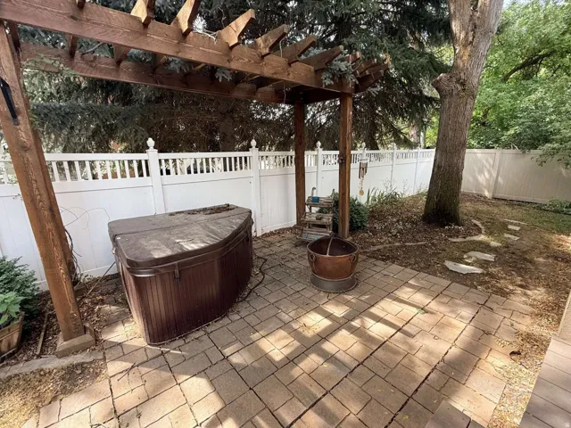 Paver patio with a wood pergola, white privacy fence, and mature trees