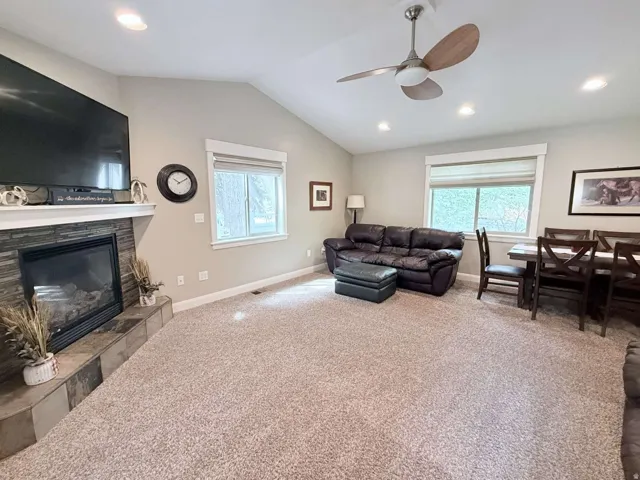 Vaulted ceiling with recessed lighting, stone-clad fireplace, ceiling fan, and large windows with blinds