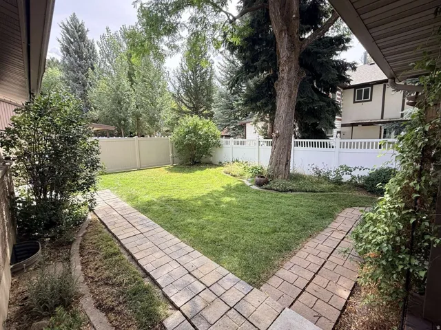 Private backyard featuring a well-maintained lawn, mature trees, and a white picket fence