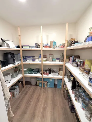 Walk-in pantry featuring multiple levels of built-in shelving, wood-finish flooring, and recessed ceiling lighting