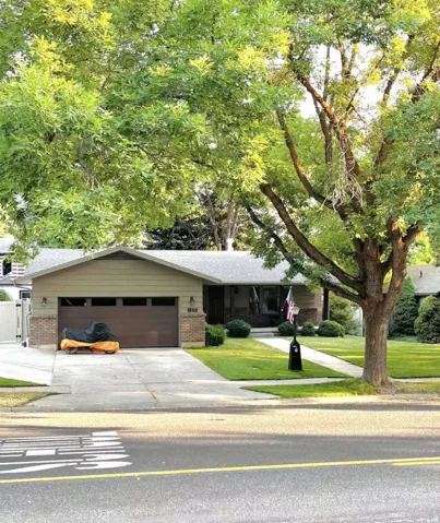 Single-story home featuring a brick and siding exterior, an attached garage with a contemporary wood-finish door, a concrete driveway, and a front lawn with mature trees and shrubs