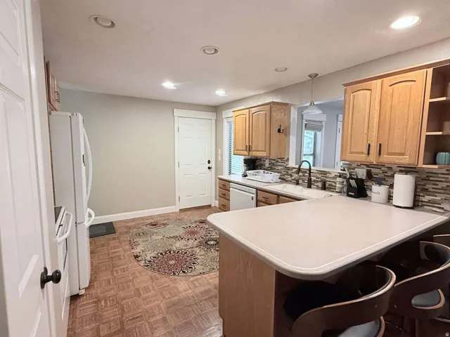 Kitchen featuring wood-finish flooring, recessed lighting, wood cabinetry, a tile backsplash, and a breakfast bar
