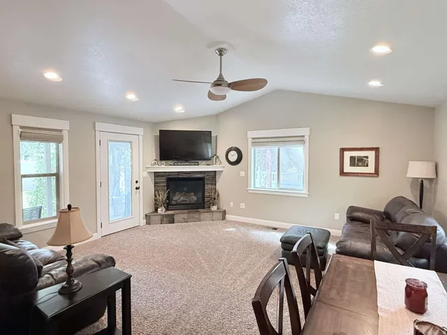 Spacious great room with recessed ceiling lighting and ceiling fan, anchored by a gas fireplace with stone surround and flat-screen TV mount