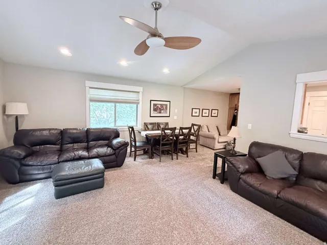 Spacious room with vaulted ceilings and recessed lighting, featuring a dining area with a wood table and chairs, and a window with a shade