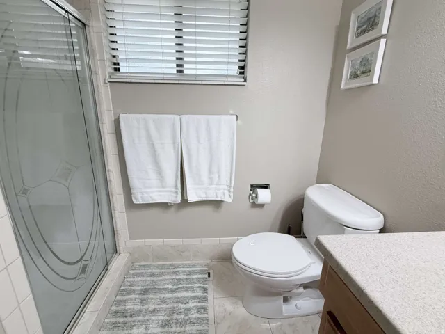 Frosted glass shower enclosure, single window with blinds, ceramic tile flooring, and integrated toilet