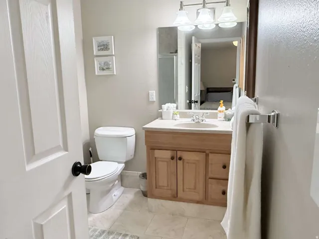 Bright bathroom featuring a wood-finish vanity with dual-sink configuration, ceramic tile flooring, and framed mirror with integrated lighting