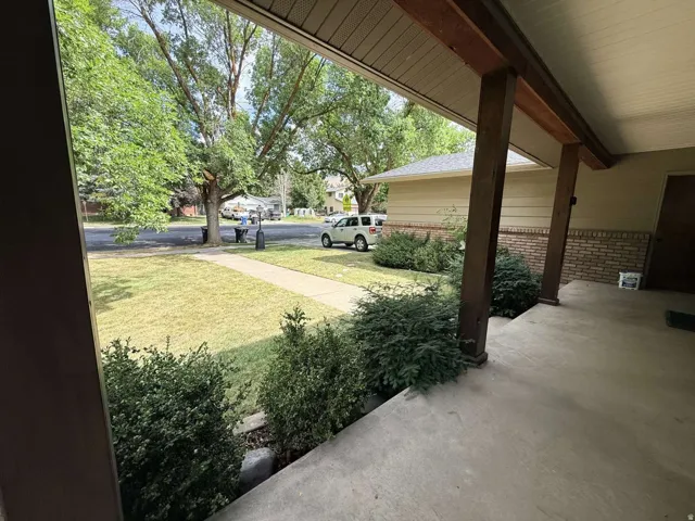 Covered concrete porch with wood posts, front yard with mature landscaping, and concrete walkway