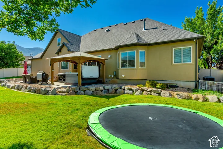 Expansive backyard featuring a stone retaining wall, level lawn, and a covered patio with a built-in spa