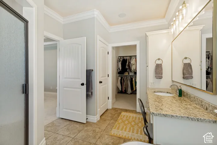 Double vanity with granite countertops, tile flooring, crown molding, and a walk-in closet