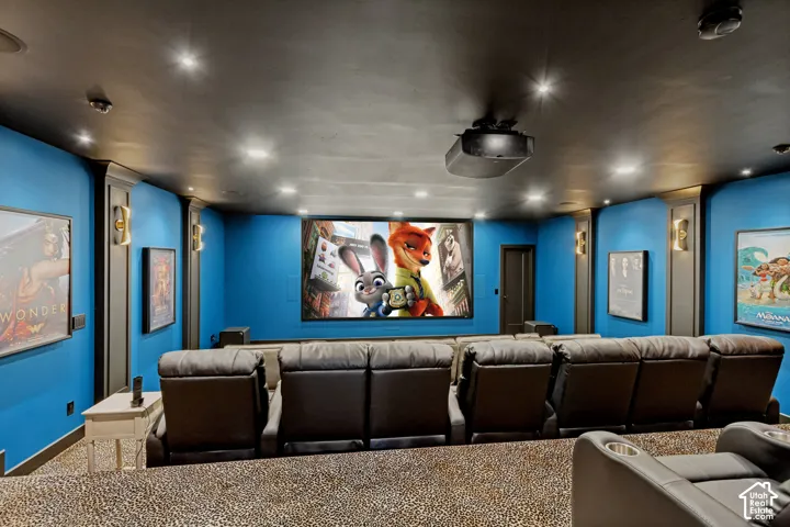 Dedicated media room featuring a projection screen, tiered seating, recessed ceiling lighting, and wall-mounted sconces