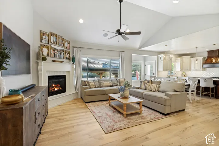 Vaulted ceiling with a ceiling fan, fireplace with mantel, light wood-finish flooring, and recessed lighting