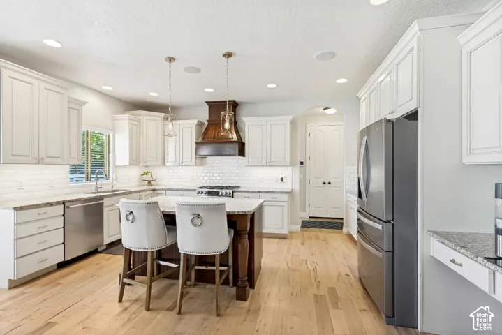 Hardwood flooring, white cabinetry, granite countertops, subway tile backsplash, and a central island with integrated storage