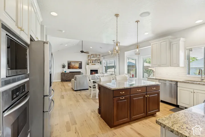 Kitchen with wood-finish flooring, stainless steel appliances, granite countertops, a central island with storage, and white cabinetry