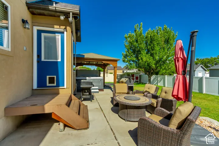 Concrete patio featuring a hot tub under a wooden gazebo, a fire pit, and a grass lawn