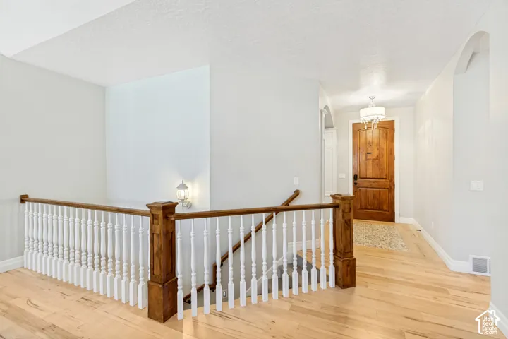 Hardwood flooring, wood newel posts, white balusters, recessed wall niche, and an ornate chandelier
