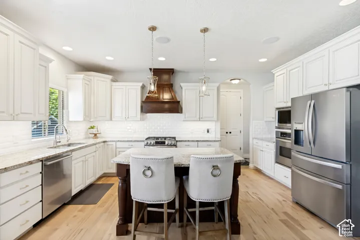 Stainless steel appliances, white cabinetry, a kitchen island with seating, pendant lighting, and wood-finish flooring