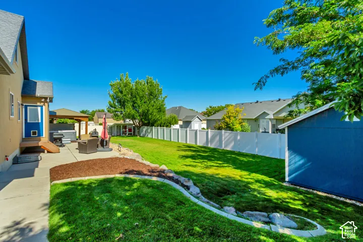Expansive backyard featuring a manicured lawn, concrete patio, privacy fencing, and a detached storage shed