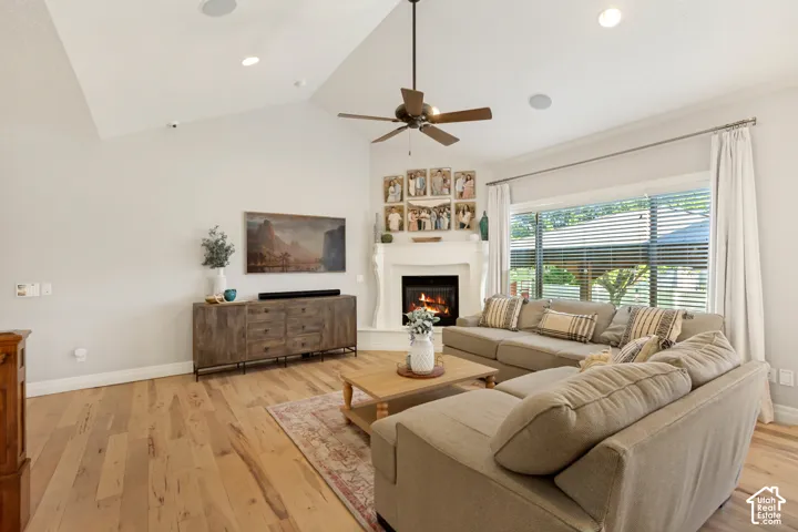 Vaulted ceiling with recessed lighting, wood-finish flooring, fireplace with white mantle, ceiling fan, and large windows