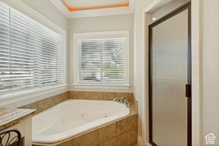Corner jetted tub with tile surround, dual windows, and an adjacent shower with a dark framed, frosted glass door