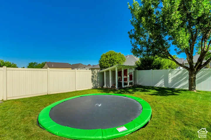 Expansive grassy backyard featuring a white privacy fence, mature tree, and a built-in outdoor structure