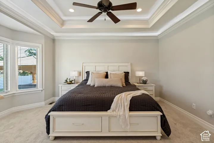 Tray ceiling with recessed lighting and crown molding, ceiling fan, bay window with blinds, and light-toned carpeting