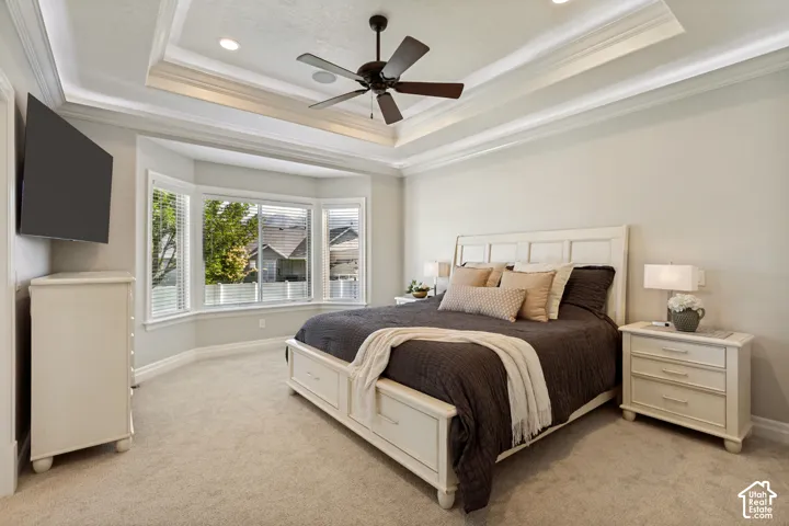 Tray ceiling with recessed lighting and a ceiling fan, bay window with blinds, and light-toned carpeting