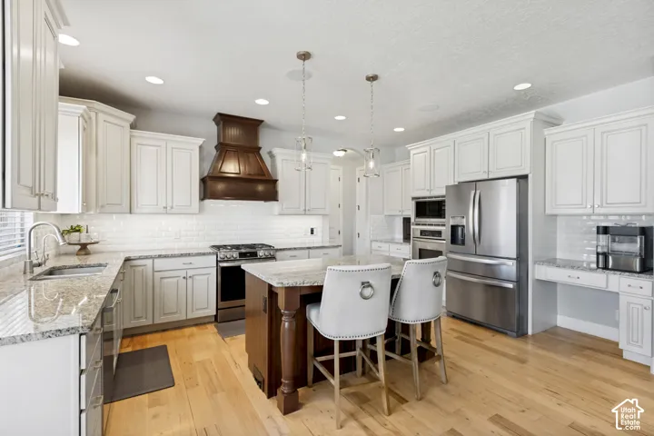 Kitchen featuring white cabinetry, granite countertops, wood-finish flooring, stainless steel appliances, and a central island with pendant lighting