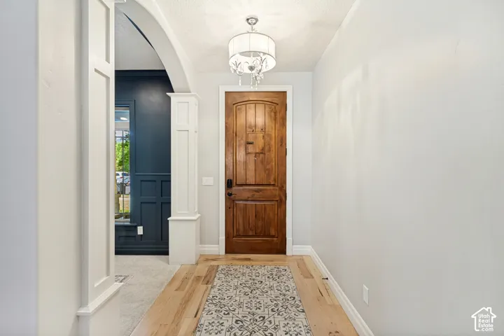 Hardwood flooring, arched doorway, decorative trim, wood paneled door, and a chandelier