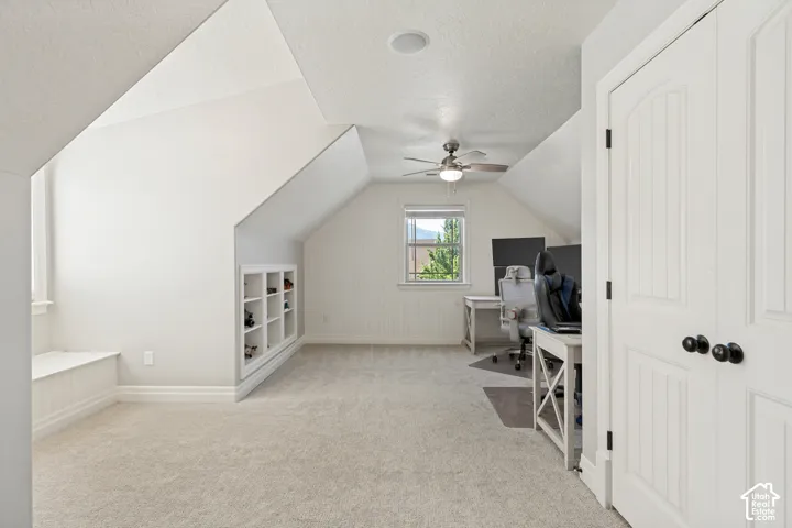 Vaulted ceiling with a ceiling fan, window with exterior scenery, built-in shelving, white paneled doors, and light-toned carpeting