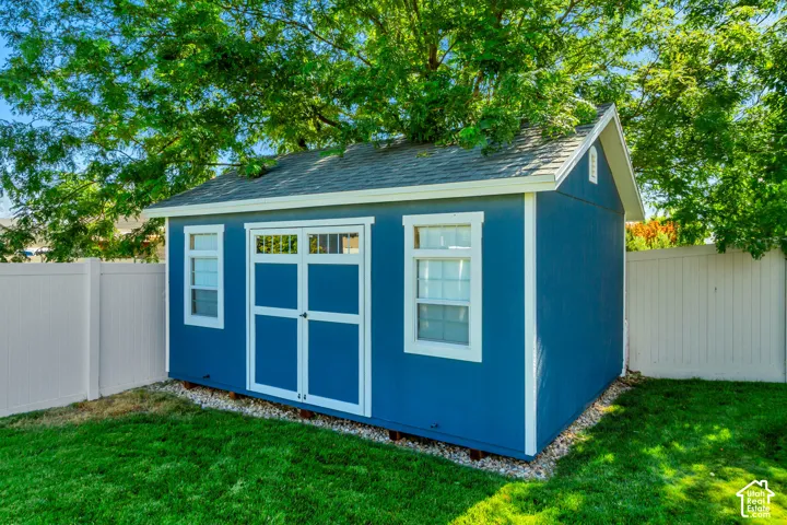 Detached storage shed with blue siding, white trim, and a shingle roof, positioned on a gravel base within a fenced yard