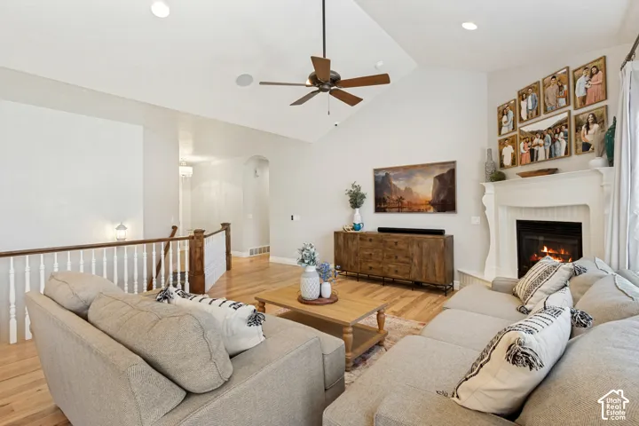 Open-concept living area featuring warm wood-finish flooring, a ceiling fan with bronze finish, and a gas fireplace with white surround and wood mantel