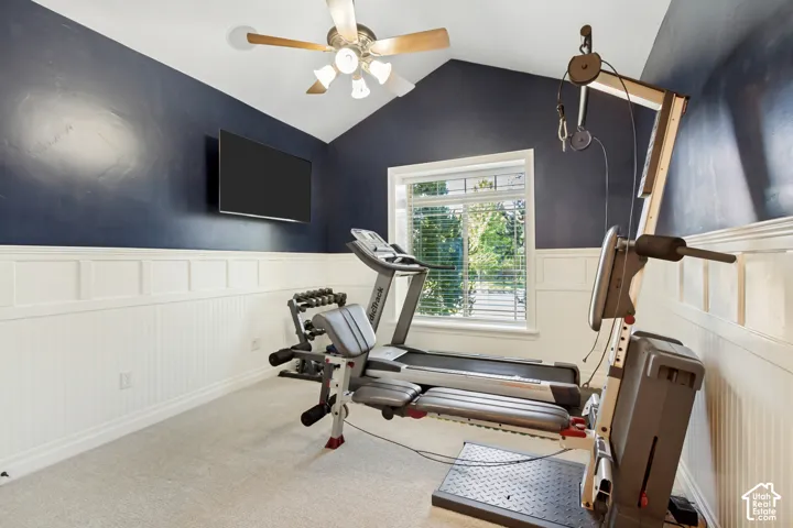 Vaulted ceiling with a ceiling fan, window with blinds, paneled wainscoting, and carpet flooring