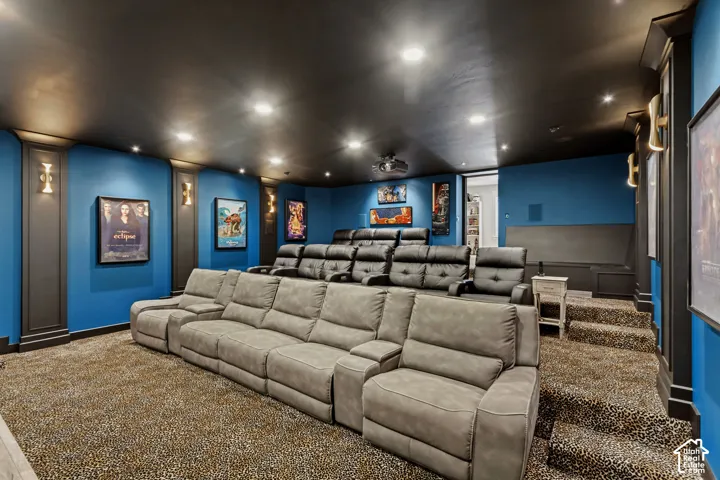 Multi-tiered seating arrangement, recessed ceiling lighting, upholstered wall panels, built-in shelving, and accent wall sconces