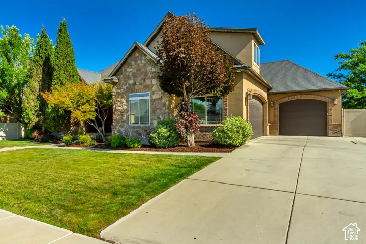 Stone and stucco exterior with multiple windows, two arched garage doors, a concrete driveway, and front lawn landscaping