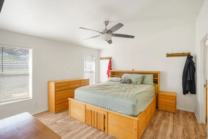 Vaulted ceiling with a ceiling fan, dual windows with blinds, and wood-finish flooring