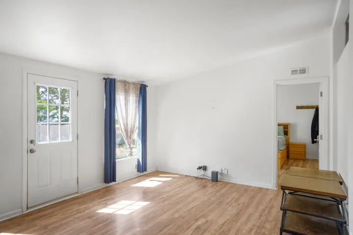 Wood-finish flooring, white walls, and a window with a curtain rod