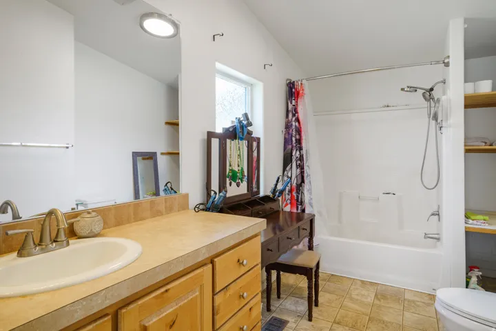 White bathtub with shower, vanity with wood-finish cabinetry, built-in shelving, and tiled flooring