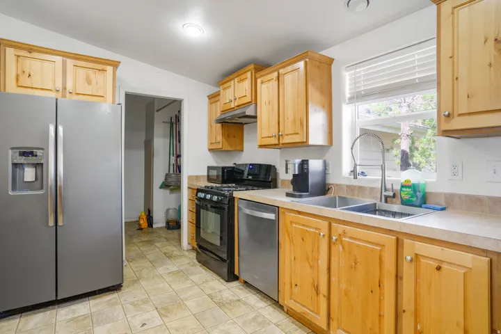 Wood cabinetry, stainless steel appliances, dual basin sink, light-toned countertops, and window with blinds