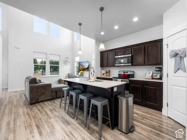 Open-concept living space featuring wood-finish flooring, a kitchen island with pendant lighting, dark wood cabinetry, and stainless steel appliances