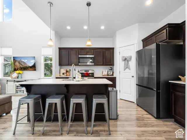 Kitchen featuring dark wood-finish cabinetry, stainless steel appliances, a center island with a light-toned countertop, pendant lighting, and wood-finish flooring