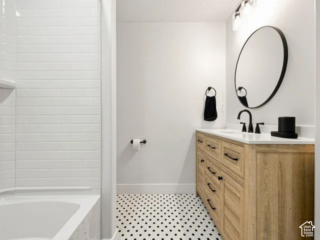 White subway tile tub surround, black and white hexagon floor tiles, wood-finish vanity with ample storage, white countertop, and contemporary black fixtures