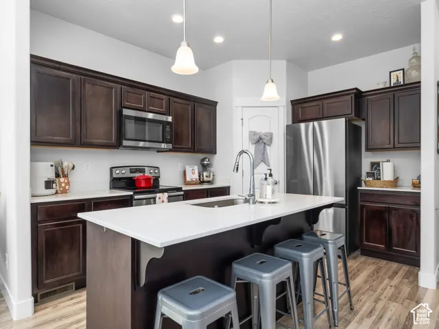 Kitchen featuring dark wood cabinetry, white countertops, stainless steel appliances, and a central island with an undermount sink