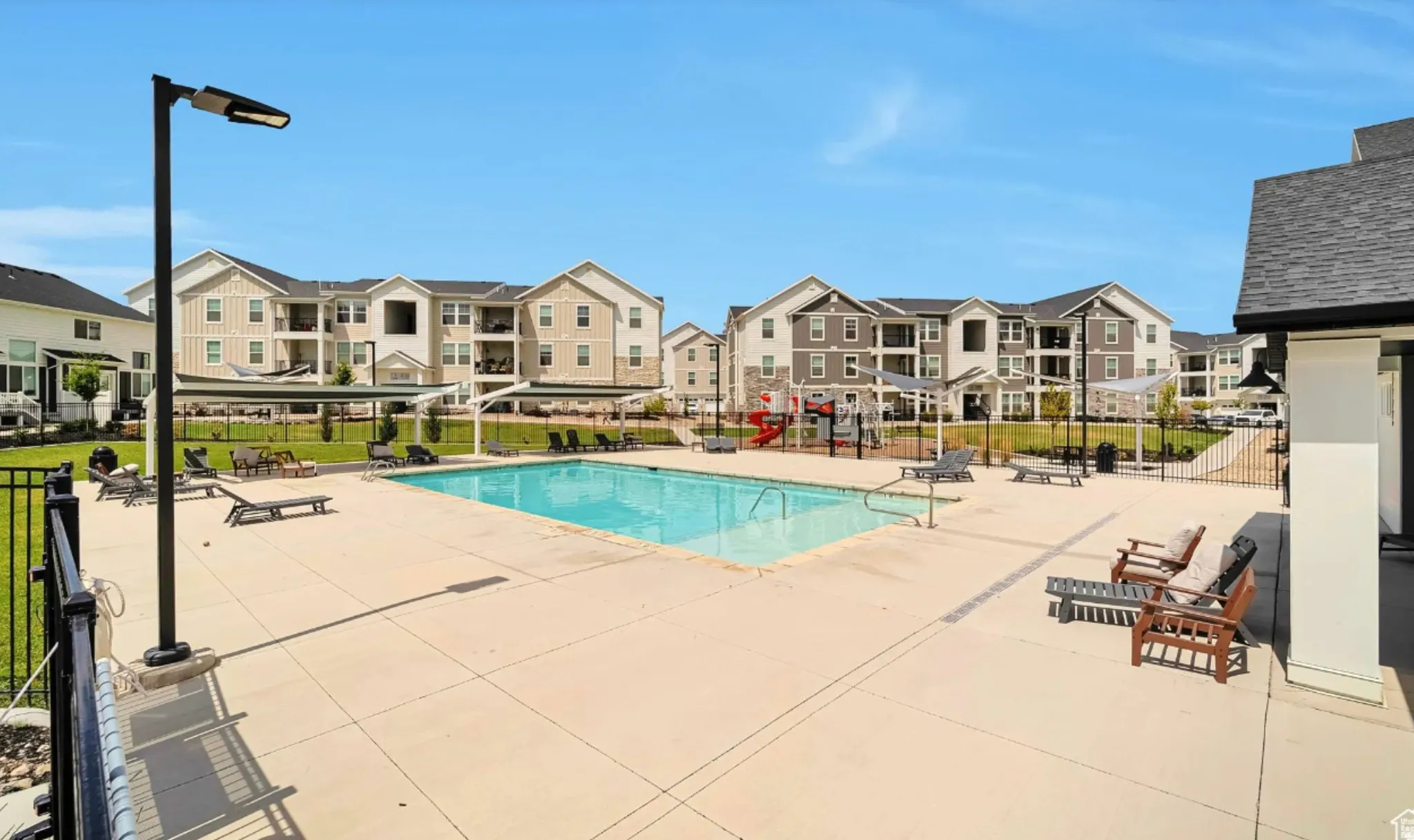 Outdoor swimming pool with concrete decking, surrounding lounge seating, and a nearby playground