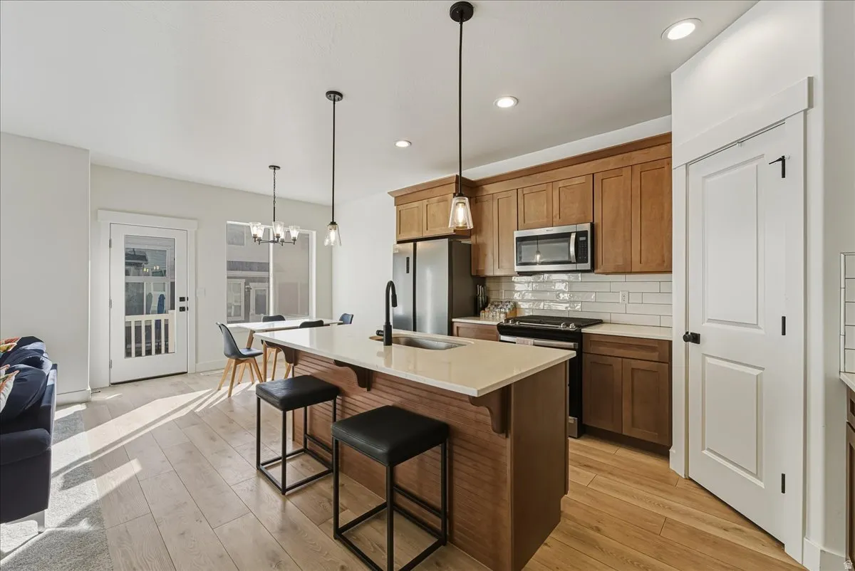 Kitchen featuring wood cabinetry, stainless steel appliances, a center island with pendant lighting, and light-tone wood-finish flooring