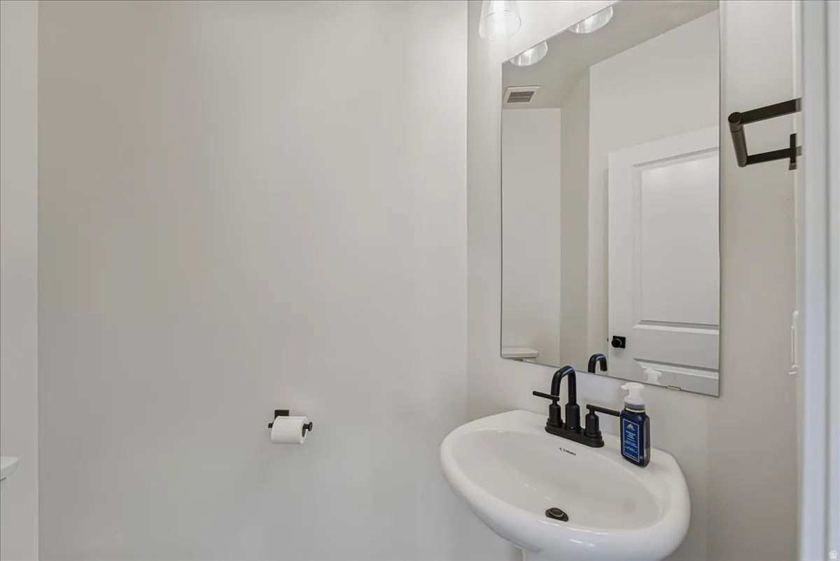Pedestal sink with a matte black faucet, wall-mounted mirror, and overhead vanity lighting