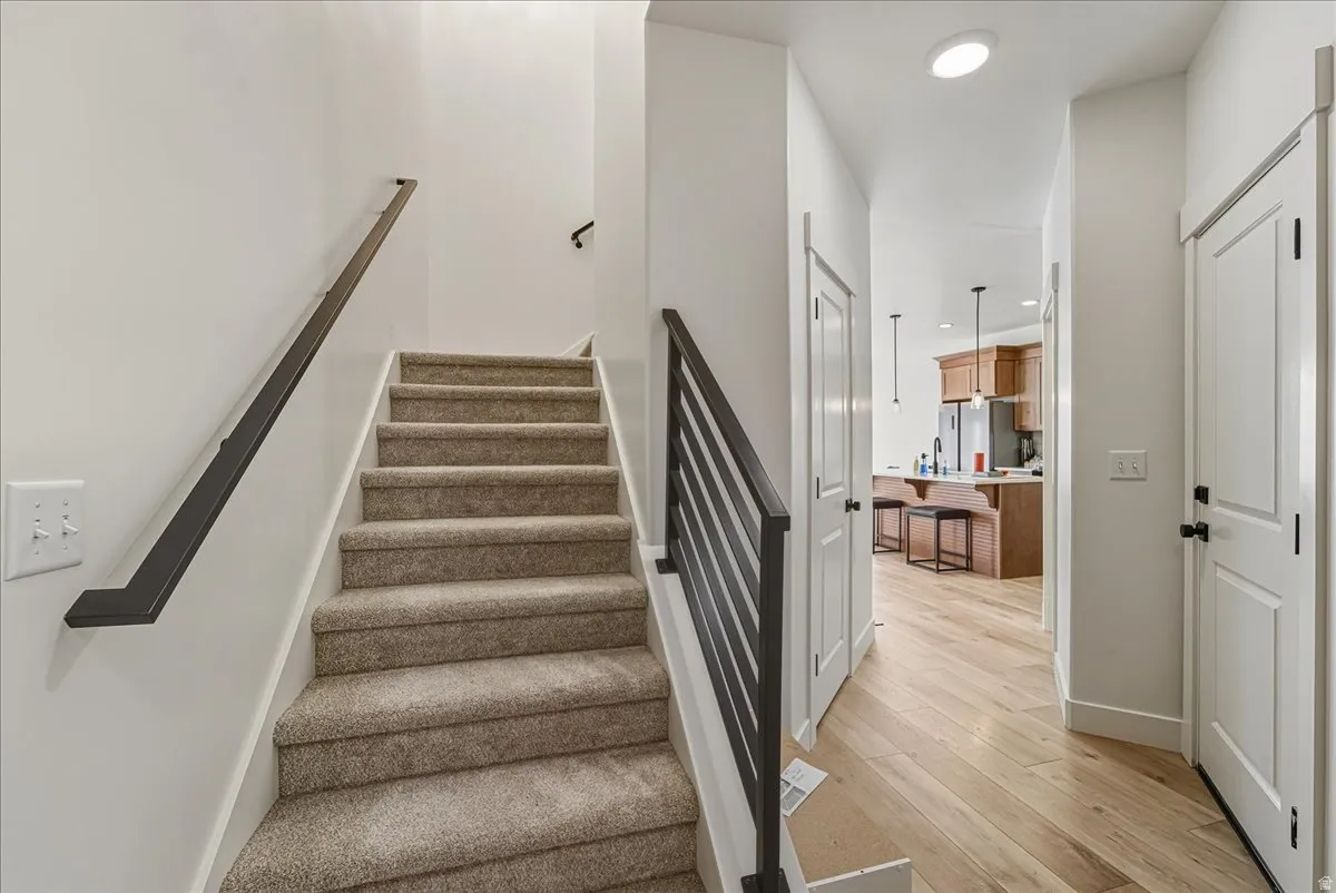Carpeted staircase with modern black metal railing, light wood-finish flooring, and recessed lighting