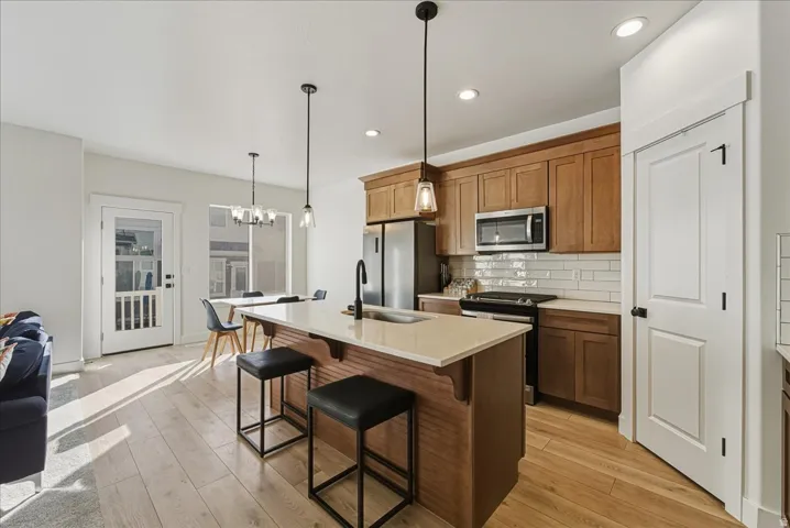 Kitchen featuring wood cabinetry, stainless steel appliances, a center island with pendant lighting, and light-tone wood-finish flooring