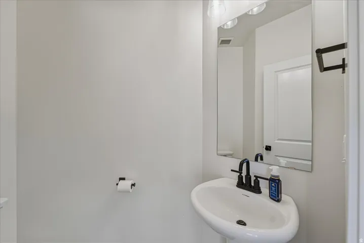 Pedestal sink with a matte black faucet, wall-mounted mirror, and overhead vanity lighting